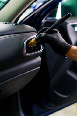 Bir oto yıkama işçisi lüks bir arabanın içini dikkatlice temizler fırça fırçası ve elektrikli süpürgeyle yakın plan temizlik yapar.