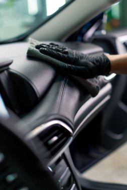 Bir oto yıkama işçisi lüks bir arabanın içini dikkatlice temizler fırça fırçası ve elektrikli süpürgeyle yakın plan temizlik yapar.