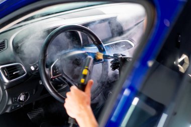 Bir oto yıkama işçisi lüks bir arabanın içini dikkatlice temizler fırça fırçası ve elektrikli süpürgeyle yakın plan temizlik yapar.