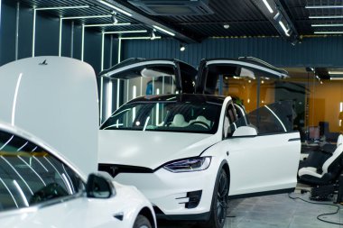 Bir araba servisinde ya da otoparkta yıkama ve kuru temizleme yaptıktan sonra açık kapısı olan lüks beyaz bir arabanın aynasını ve farını detaylandırmak.