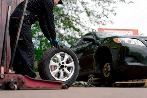 汽车修理工在街上的轮胎车间里用钻头把一辆黑色汽车的轮子换了下来 详细说明了汽车修理的情况 — 图库照片
