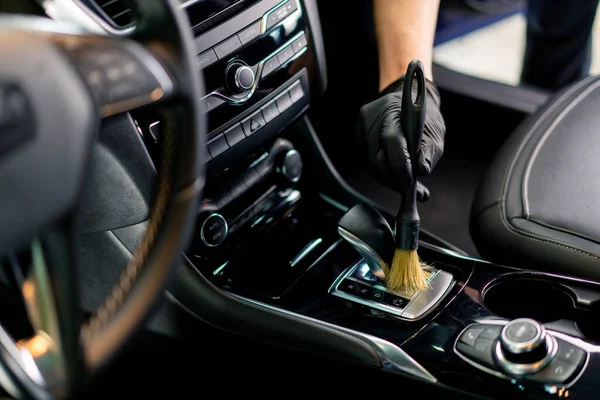 A car wash worker carefully cleans the interior of a luxury car with a rag a brush vacuum cleaner steamer detailing close-up