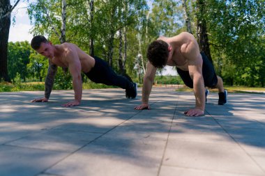 Genç sporcular antrenman sırasında sokaklarda şınav çekiyorlar. Kollar ve omuzlar seksi.