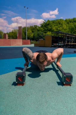 Pompalı genç sporcu sokak antrenmanı sırasında yerden şınav çekiyor. Kollarını sallıyor.