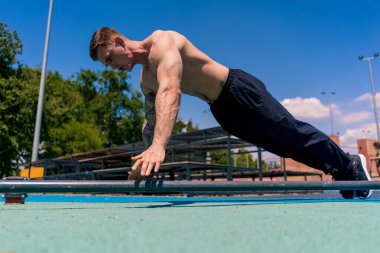 Pompalı genç sporcu sokak antrenmanı sırasında yerden şınav çekiyor. Kollarını sallıyor.