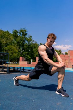 Genç şişirilmiş sporcu vücut geliştirici sokak sporları sahasında bacak hareketleri yapıyor.