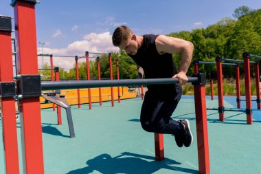 Paralel barlarda çalışan genç bir sporcunun portresi. Kollarını ve omuzlarını sallayarak sokak antrenmanı sırasında şınav çekiyor.