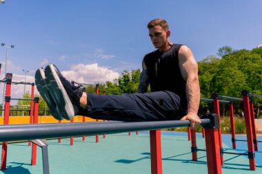 Paralel barlarda çalışan genç bir sporcunun portresi sokak antrenmanı sırasında basını sallıyor ve spor sahasında şınav çekiyor.