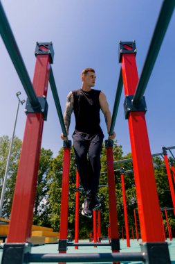 Paralel barlarda çalışan genç bir sporcunun portresi. Kollarını ve omuzlarını sallayarak sokak antrenmanı sırasında şınav çekiyor.