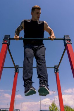 Genç terli sporcunun portresi yatay bar hareketleri yapıyor kollarını ve omuzlarını sallıyor sokak eğitimi sırasında.