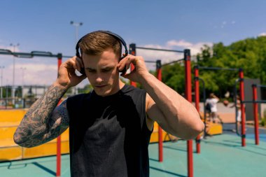 Spor sahasında parkta motivasyon eğitimi alan dövmeli ve piercingli terli genç bir sporcunun portresi.