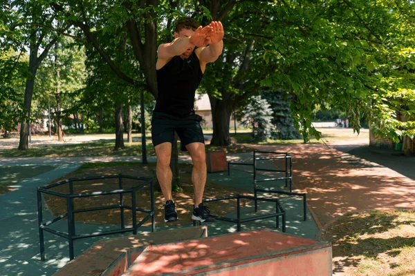 young fitness sportsman jumps on a box with both feet, performs a workout at sports street workout