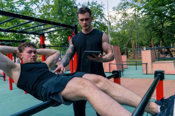 Trener Fitness Tabletem Ręku Trenuje Młodego Sportowca Pompującego Swoje Mięśnie — Zdjęcie stockowe