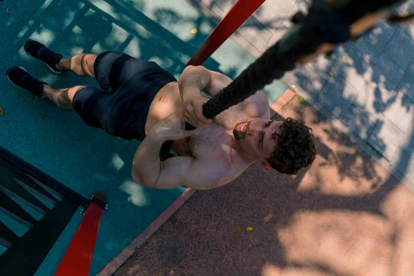 在运动场进行户外运动时 一个赤身裸体的年轻运动员拉上绳子 性感地把身体抽上来 — 图库照片
