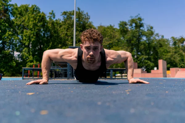 young pumped-up athlete doing push-ups from the ground during street training endurance exercise swings arms shoulders