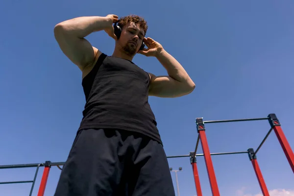 portrait of a young sweaty sportsman listening to music in headphones on a sports ground during outdoor training bottom view