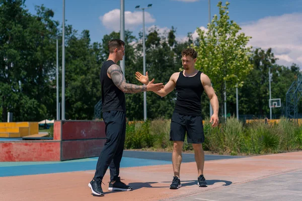 Personal fitness trainer and young sportsman are greeting each other on sports ground Two active guys before starting training