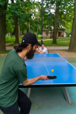 Engelli bir adama karşı masa tenisi oynayan yaşlı adam şehir parkında tekerlekli sandalyede oturuyor.