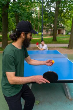 Engelli bir adama karşı masa tenisi oynayan yaşlı adam şehir parkında tekerlekli sandalyede oturuyor.