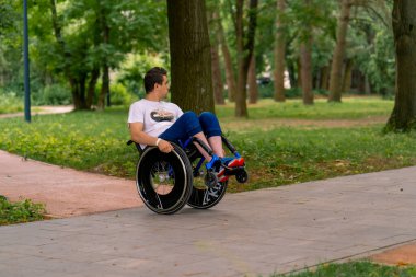 Özürlü bir adam şehir parkında ağaçlara karşı tekerlekli sandalye dublörlüğü yapar.