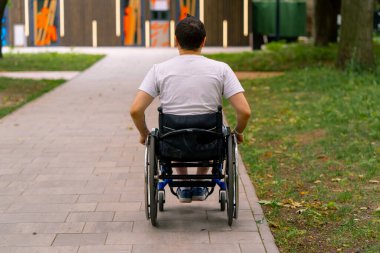 Özürlü bir adam, arka plandaki ağaçlara karşı şehir parkı yolunda tekerlekli sandalyeye biner.