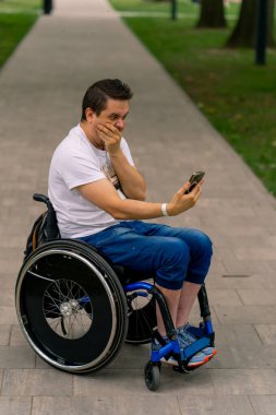 Tekerlekli sandalyedeki engelli bir adam akıllı telefona bakar ve şehir parkında ne tuttuğuna hayret eder.