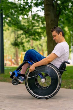 Özürlü bir adam şehir parkında ağaçlara karşı tekerlekli sandalye dublörlüğü yapar.