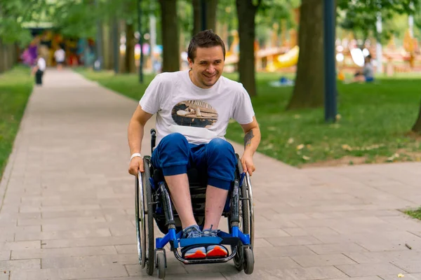 包括性 障害のある男性は 木の背景に沿って市立公園のパスに沿って車椅子に乗ります — ストック写真