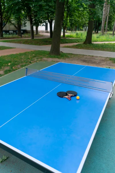 Две Теннисные Ракетки Оранжевый Теннисный Мяч Лежат Синем Теннисном Столе — стоковое фото