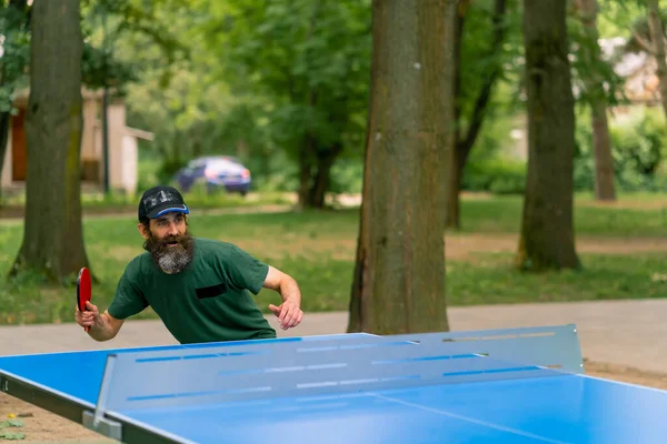 在城市公园里 一位头发长且胡须灰白的老人在打乒乓球 — 图库照片
