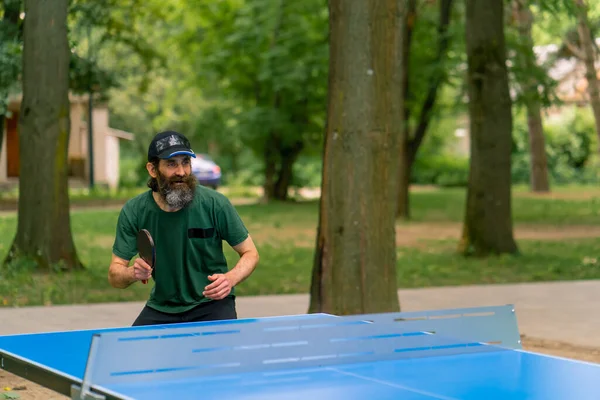 在城市公园里 一位头发长且胡须灰白的老人在打乒乓球 — 图库照片