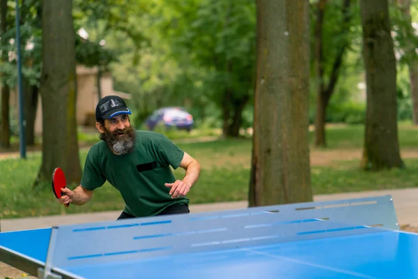 包容性 長髪の高齢者に焦点を当てた男と 都市公園で灰色のひげがピンポンを演じる — ストック写真