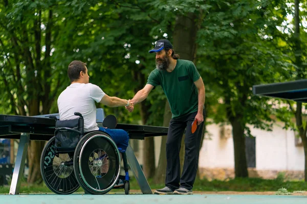 在乒乓球比赛之前 一位手握网球拍的全能型残疾人与一位年长的男子握手 — 图库照片