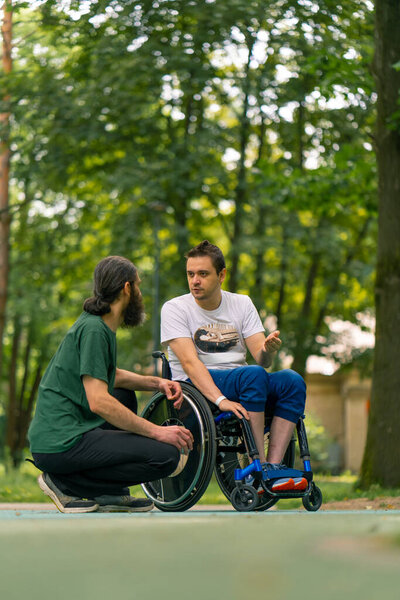 Inclusiveness A man with disabilities communicates with an elderly man with long hair and gray beard in city park with trees in the background