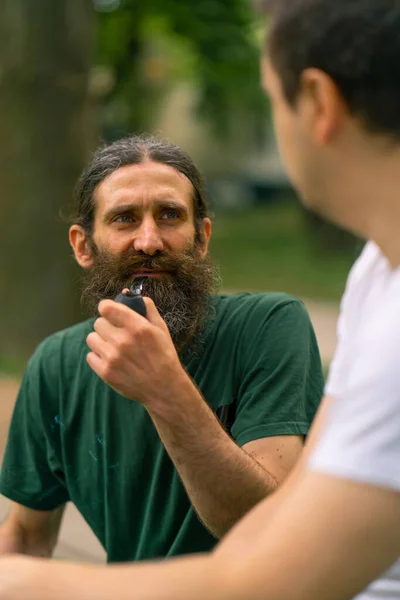 包括性 障害のある男性は 木の背景から都市公園でパイプを喫煙する高齢者と相互作用します — ストック写真