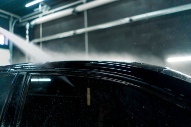 Çatıya yakın çekim ve araba yıkama yerinde yüksek basınçlı siyah bir araba camı.
