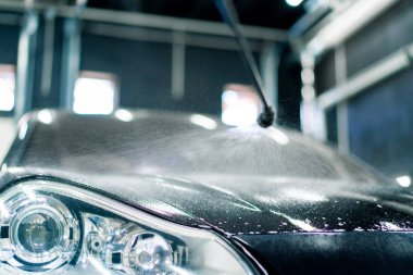 Araba yıkama kutusundaki bir sprey şişeden araba yıkama makinesinin ön farını kapatırken.