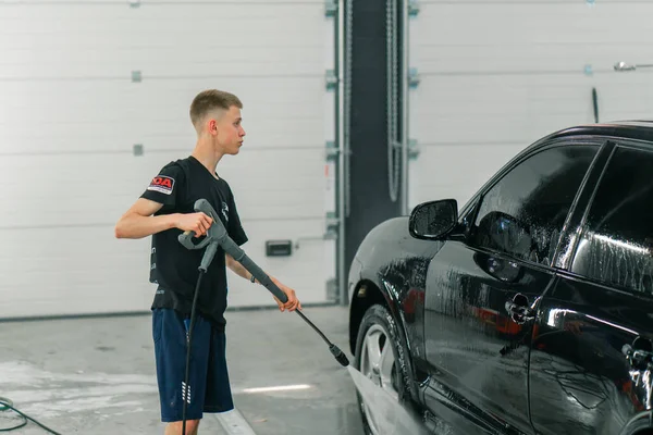男性の洗車員が洗車場で高圧洗濯機で黒い高級車を洗浄する — ストック写真
