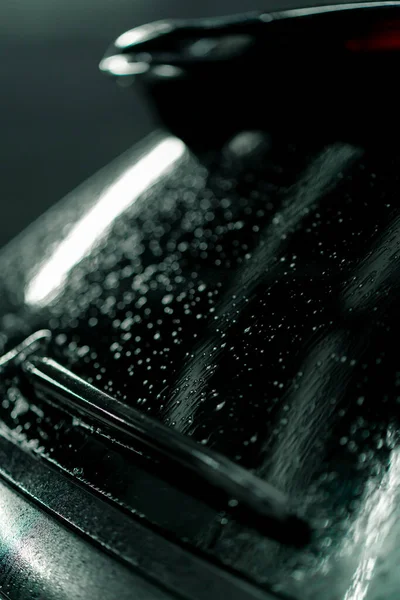 Close-up of the rear window of a black car at the moment of applying car wash from a spray bottle in car wash box