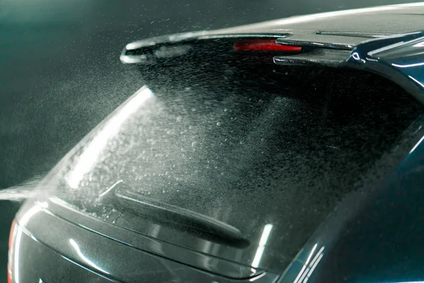Close-up of the rear window of a black car at the moment of applying car wash from a spray bottle in car wash box