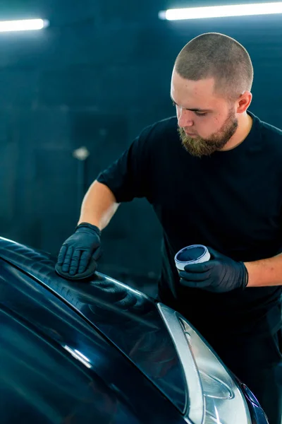 一位戴着黑色手套的洗车工人用海绵擦亮了一辆豪华黑色汽车的车篷和前灯 — 图库照片