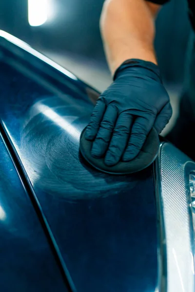 黒い手袋の洗車労働者のクローズアップ 車の磨くスポンジが付いている豪華な黒い車のフードそしてヘッドライトを磨きます — ストック写真
