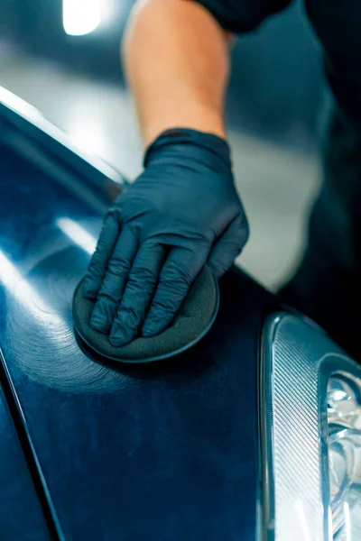 黒い手袋の洗車労働者のクローズアップ 車の磨くスポンジが付いている豪華な黒い車のフードそしてヘッドライトを磨きます — ストック写真