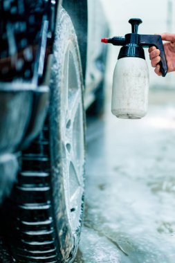 Sprey tabancadan siyah lüks arabanın tekerleğine kadar araba yıkama ürününün yakın çekimi.