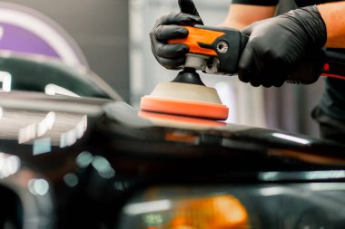 Siyah lüks arabanın kaputunu cilalamak için bir cilalama makinesi kullanan bir oto yıkama işçisinin yakın çekimi.