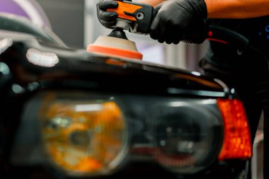 Siyah lüks arabanın kaputunu cilalamak için bir cilalama makinesi kullanan bir oto yıkama işçisinin yakın çekimi.