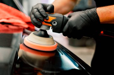 Siyah lüks arabanın kaputunu cilalamak için bir cilalama makinesi kullanan bir oto yıkama işçisinin yakın çekimi.