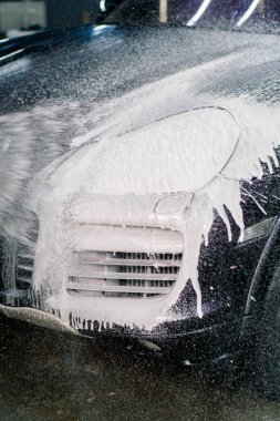 Ön farlarda araba köpüğü ve araba yıkama kabininde siyah lüks bir arabanın tamponu.