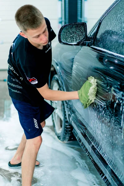 男性の洗車労働者は洗車シャンプーで黒い高級車を洗浄するために緑の洗濯布を使用します — ストック写真