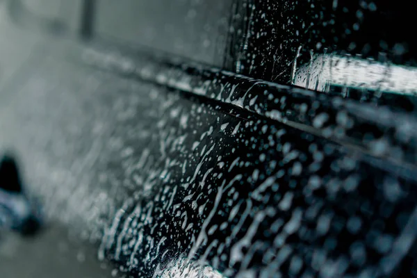 a close-up of the windshield and interior of a luxury car at the moment of car wash using foam and pressure washer